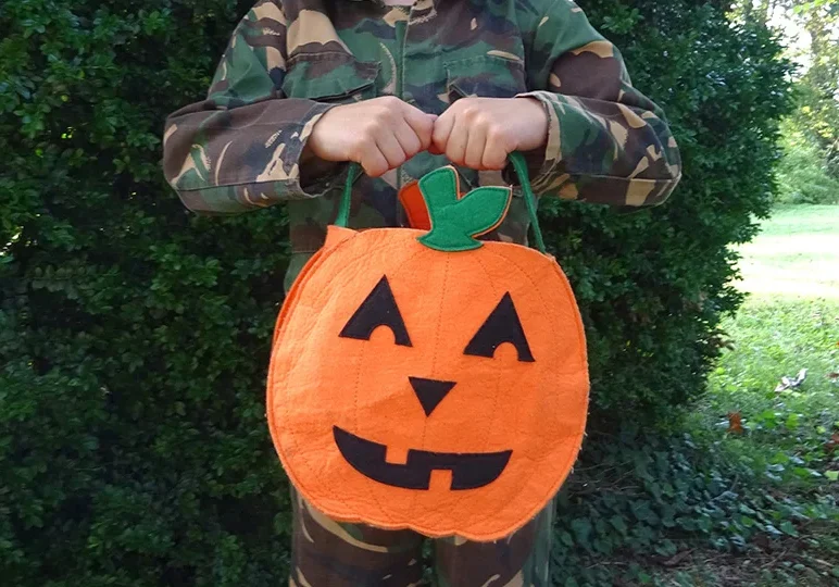 A person in camouflage holding an orange bag.